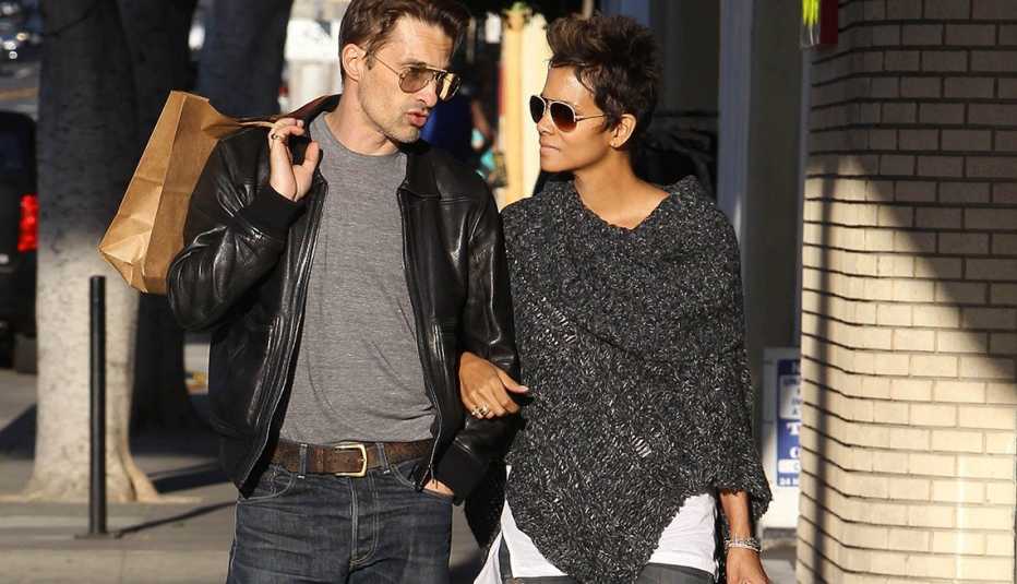 Halle Berry wearing a gray poncho sweater, walks down a sidewalk with friend