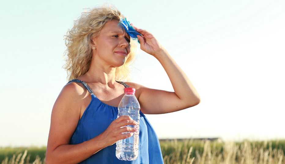 A woman wiping her forehead with a paper tissue while holding a water bottle outside