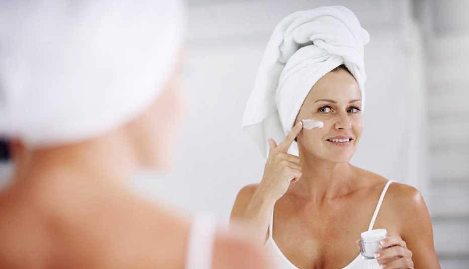A woman applying moisturizer to her face in front of a mirror