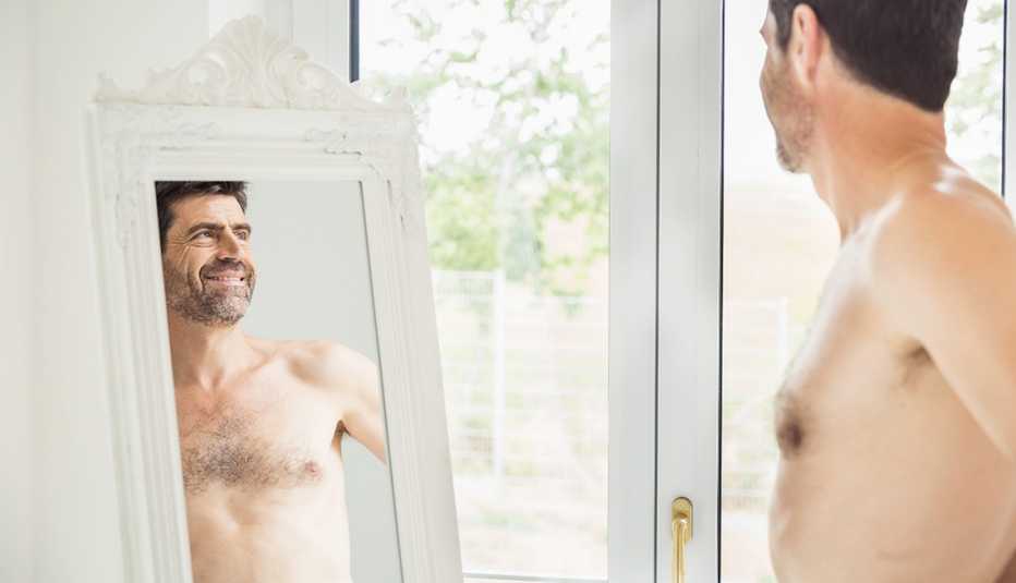 A shirtless man looking at himself in a full length mirror at home
