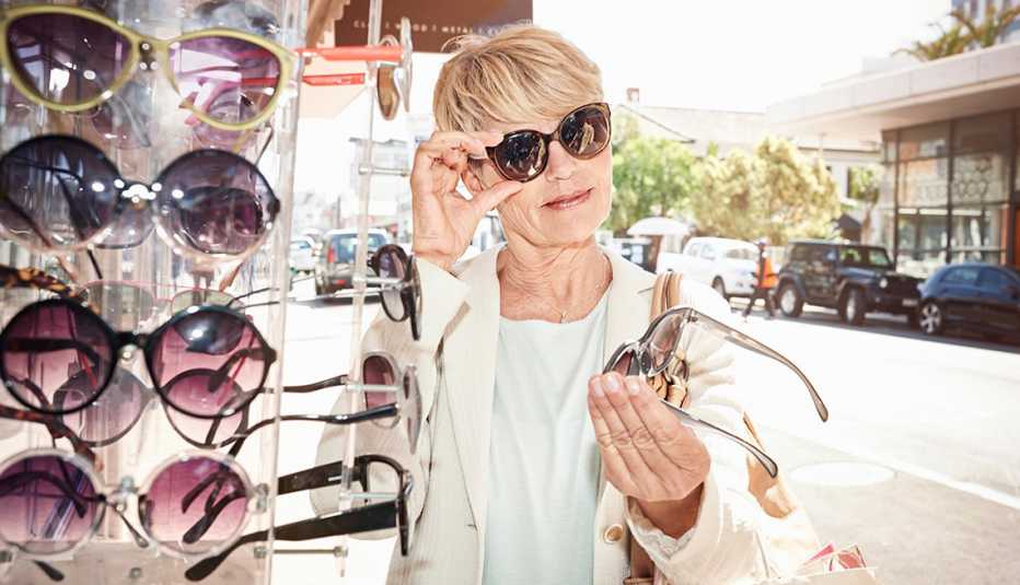 A woman is trying on sunglasses and examining another pair in her hand