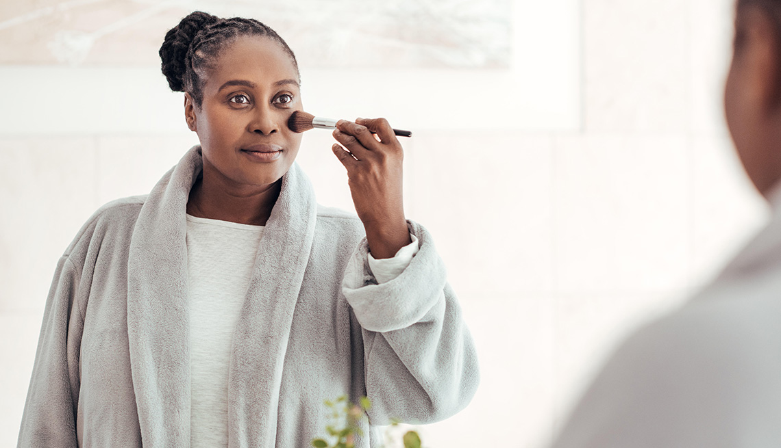A woman applies foundation on her face with a brush