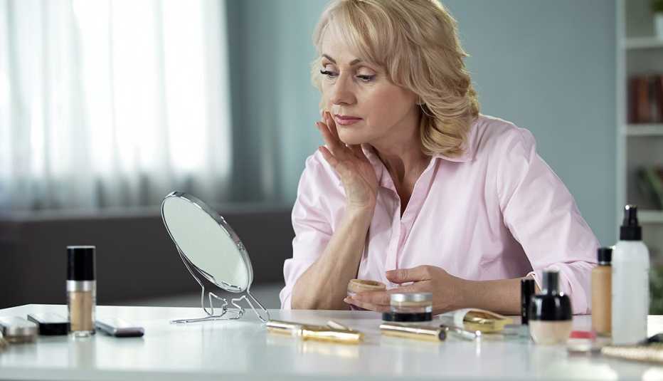 Woman applying makeup in front of a small mirror on a desk