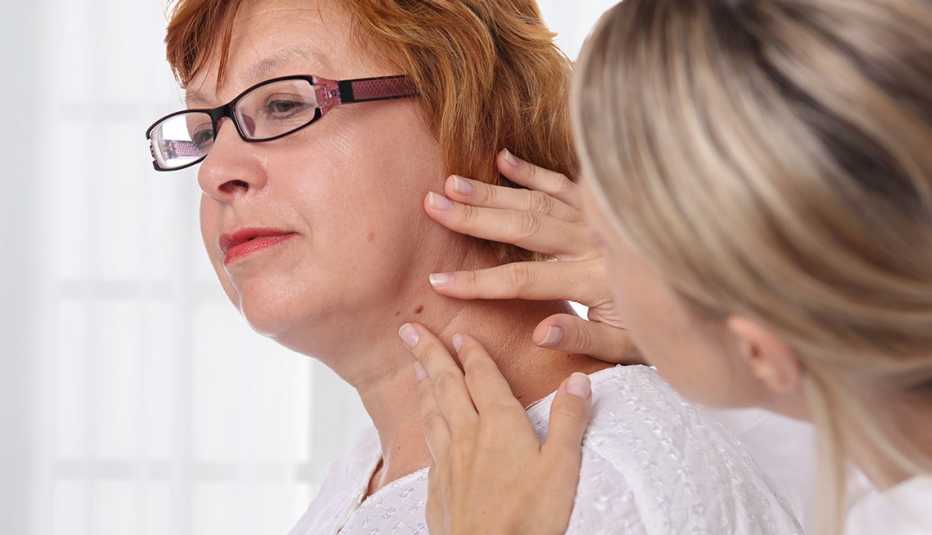 A dermatologist checking a dark spot in the area of a female patient's face and neck area