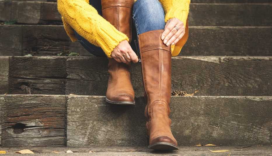 A woman sitting on the stairs and fastening the zipper on her brown leather boots