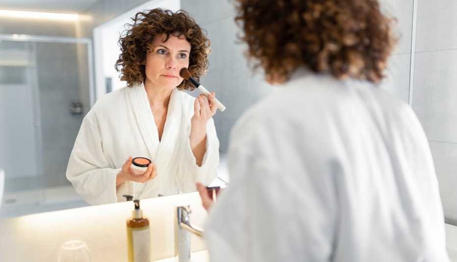A woman using a brush to apply makeup in front of a bathroom mirror