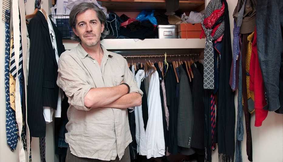 A man with his arms crossed standing in front of a closet full of clothes