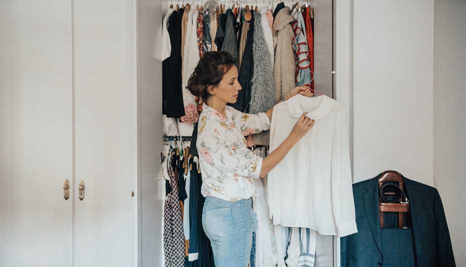 A woman looking at a white shirt in front of her closet