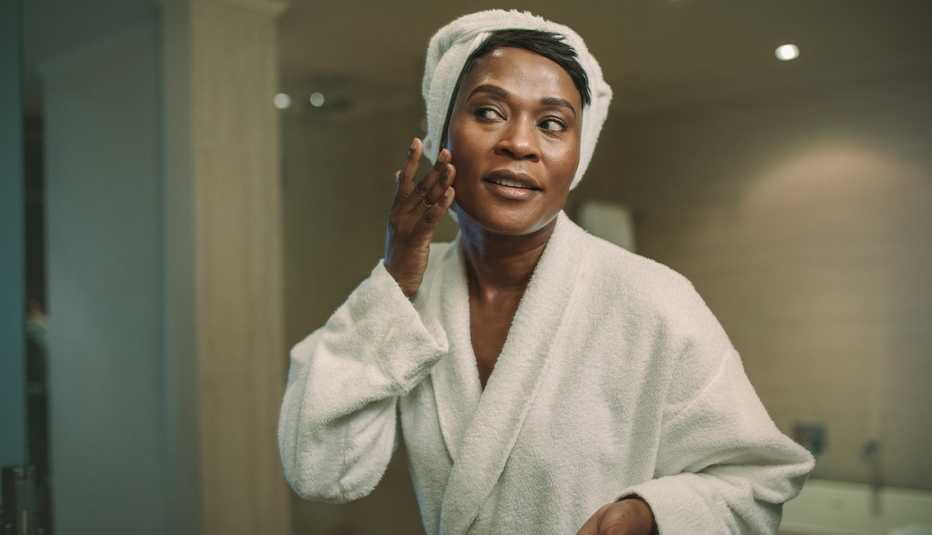 A woman applying lotion on her face in front of a bathroom mirror