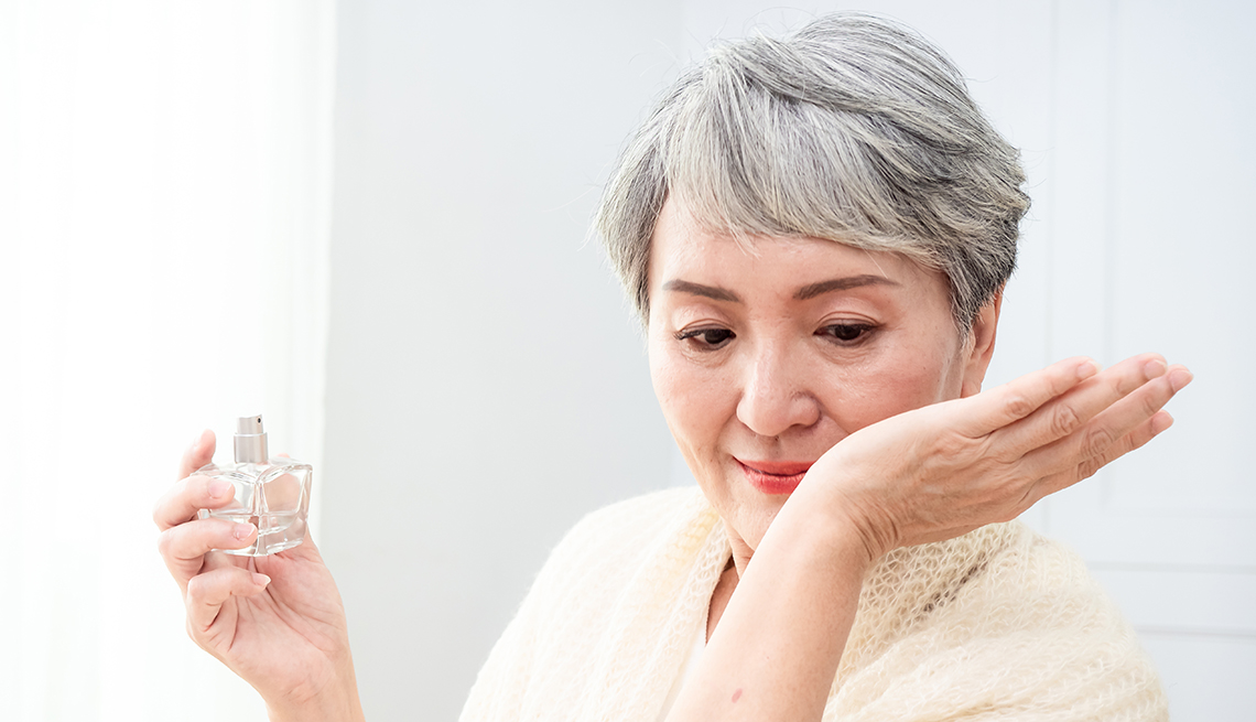 Woman sniffing her wrist after applying scent, holding perfume bottle in other hand