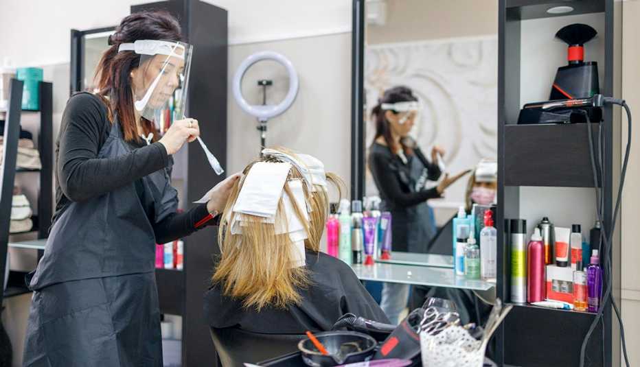 A hair dresser applying highlights to a customer sitting in a chair in front of a mirror