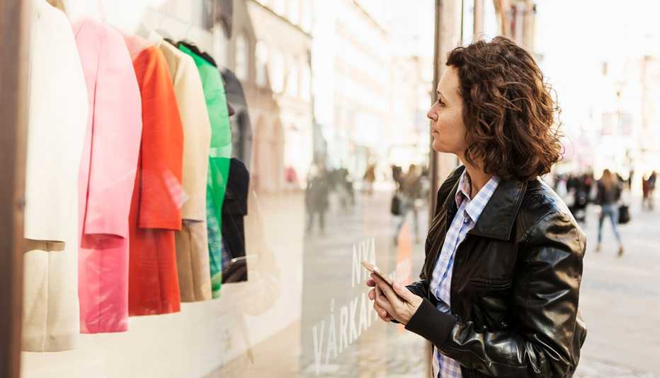 A woman looking at clothes through a window display outside of a store