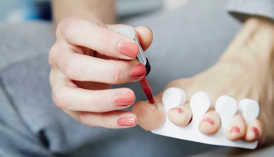 A close up of a woman painting her toenails while doing a pedicure at home