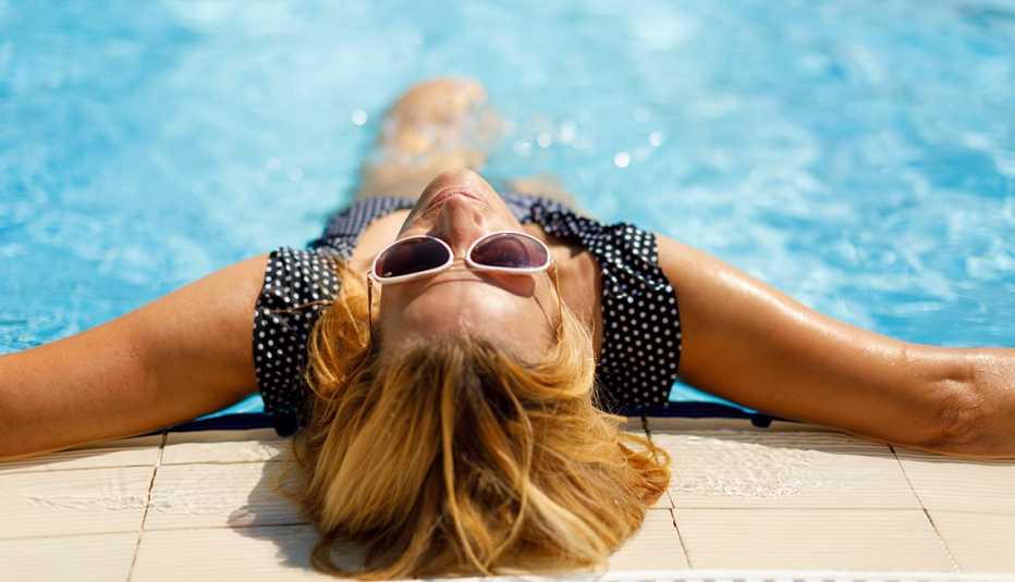 a relaxed woman wearing sunglasses leaning back against the wall of a swimming pool