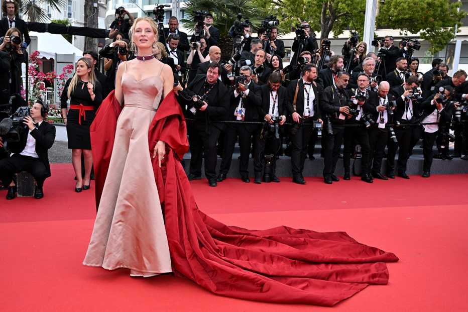 Uma Thurman wearing a taupe spaghetti strap gown with a scarlet opera coat and large train at the 76th Annual Cannes Film Festival