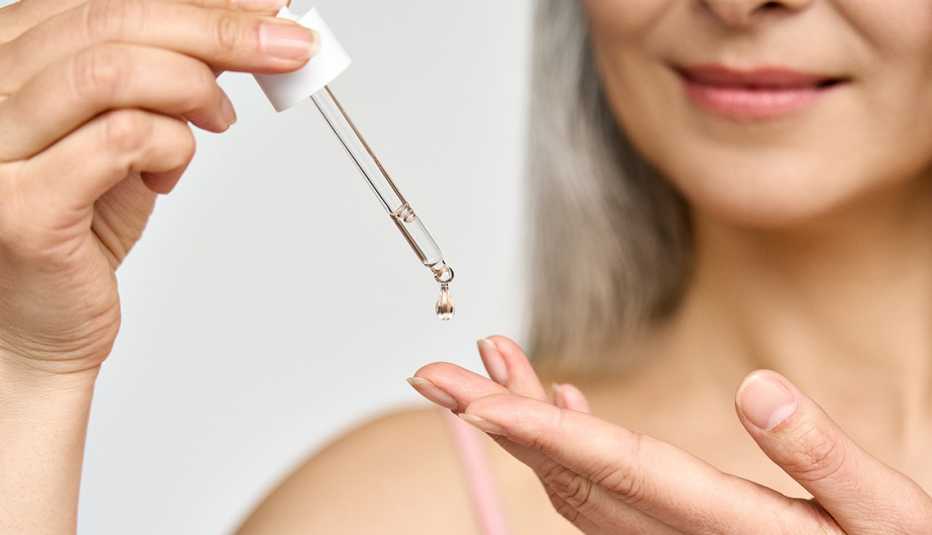 closeup of a woman holding a skin serum bottle dropper and putting some on her fingers to spread on her face 