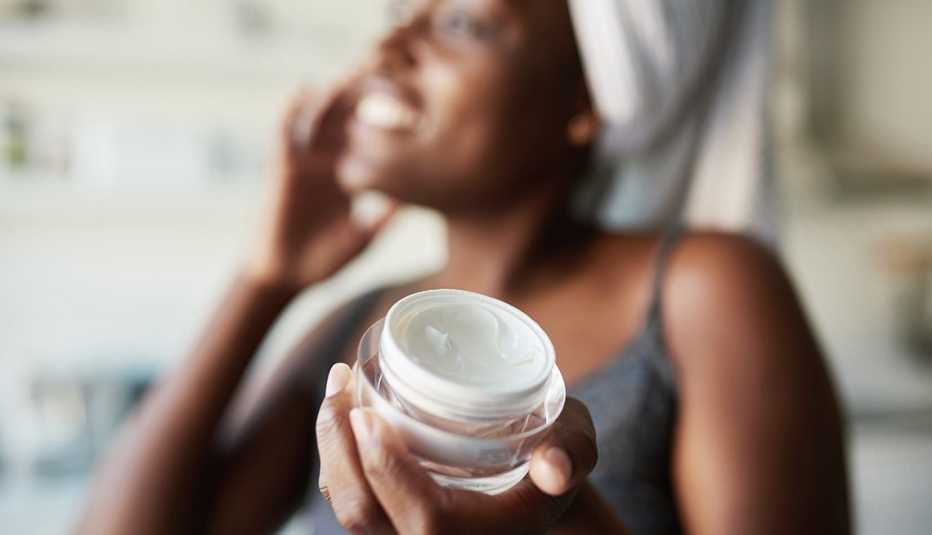 a woman applies a facial product while holding out the container