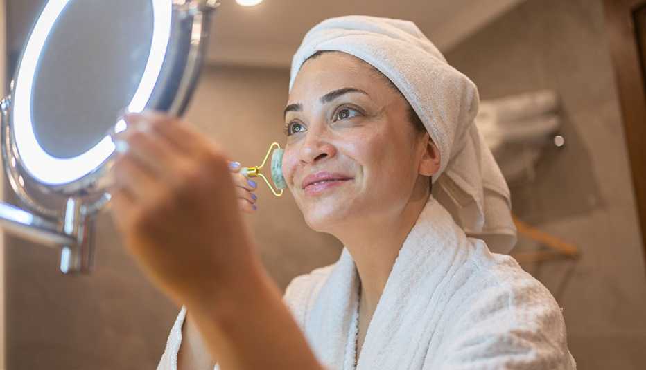a woman in a bath robe using a jade roller on her face