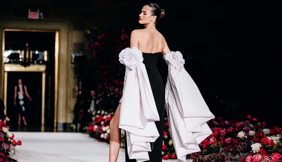 A model on the runway turned with her back showing her wearing a black dress with two white bows on her arms at Christian Siriano RTW Fall 2023 fashion show