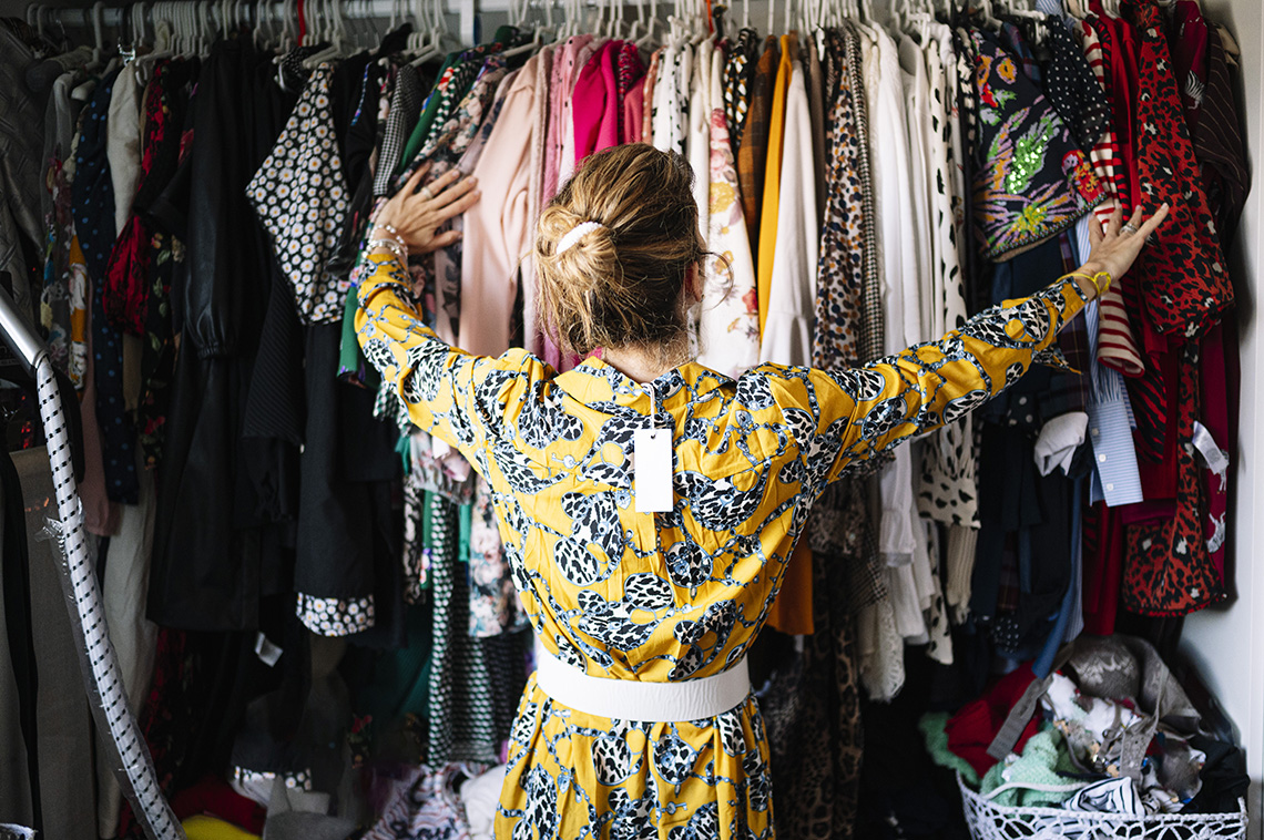 A woman in a yellow dress with its price tag looking at a closet full of clothes