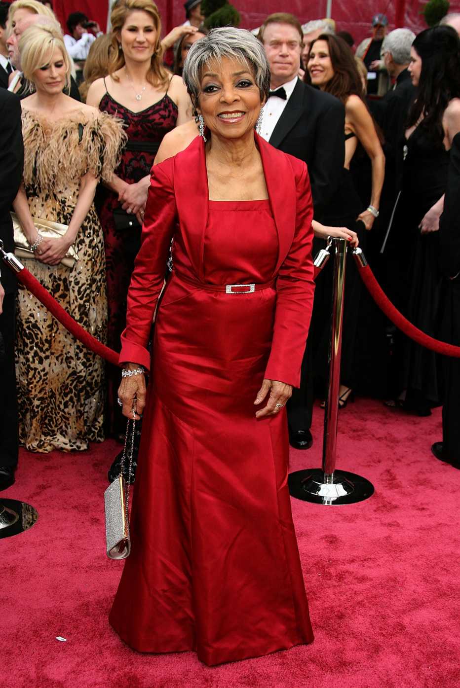 Ruby Dee on the red carpet wearing a red long sleeved belted gown at the 80th Annual Academy Awards