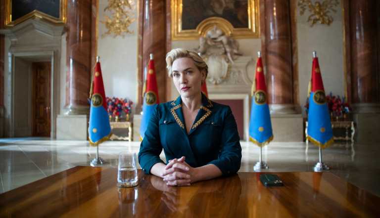 Kate Winslet sitting at a table with a glass of water nearby in the HBO series "The Regime."