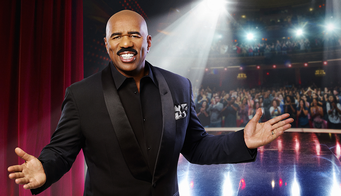 portrait of steve harvey with arms outstretched on a stage with audience behind