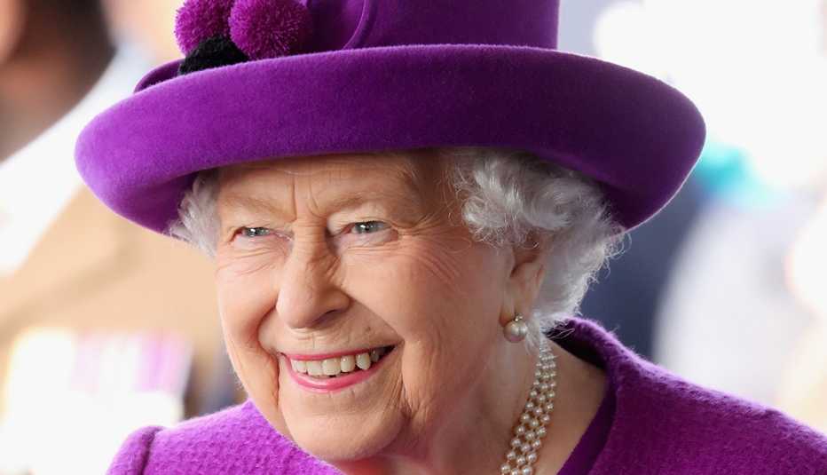 Queen Elizabeth II wearing a purple hat smiling as she visits the Royal British Legion Industries village