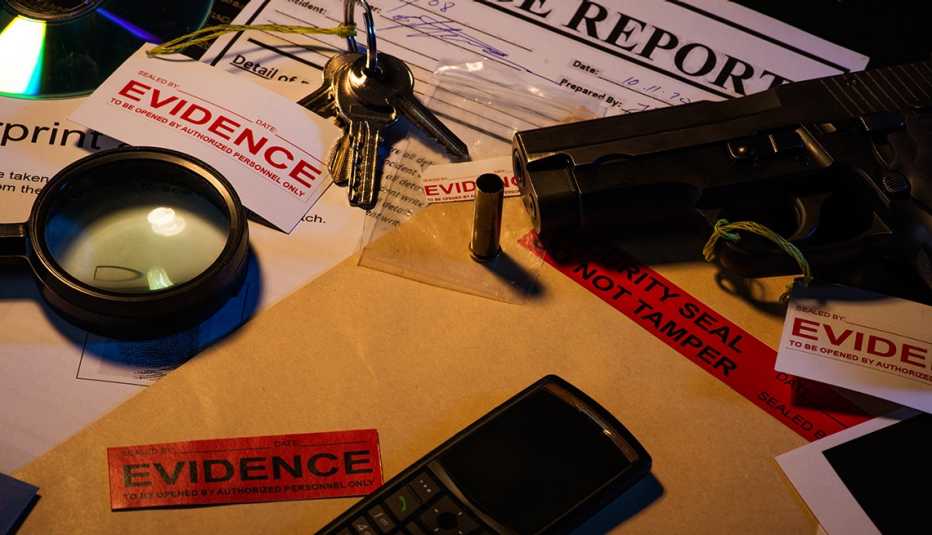 A desk with evidence from a crime case that includes a gun blank photos crime scene information sheet c d, magnifying glass keys cell phone bullet shell and police reports