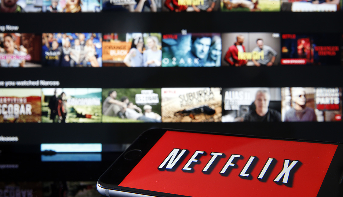 The Netflix logo is displayed on a smartphone in front a television screen that's on the streaming service's home page