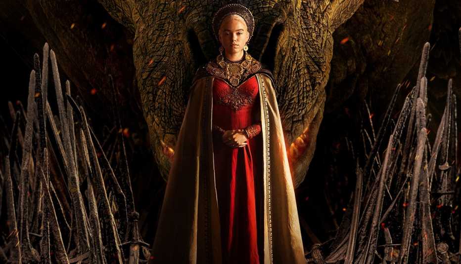 Milly Alcock as Young Rhaenyra standing in front of a dragon in promotional art for House of the Dragon