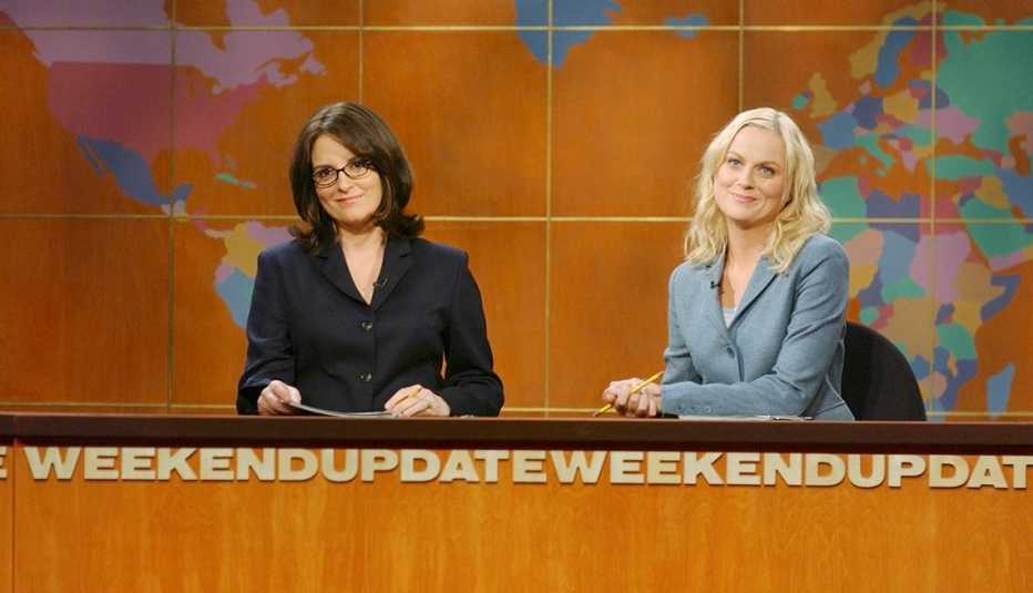 Tina Fey and Amy Poehler sitting at the anchor desk during Weekend Update on Saturday Night Live