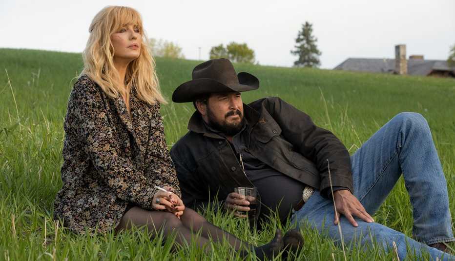 Kelly Reilly and Cole Hauser sitting on the grass in a scene from Season 5 of Yellowstone