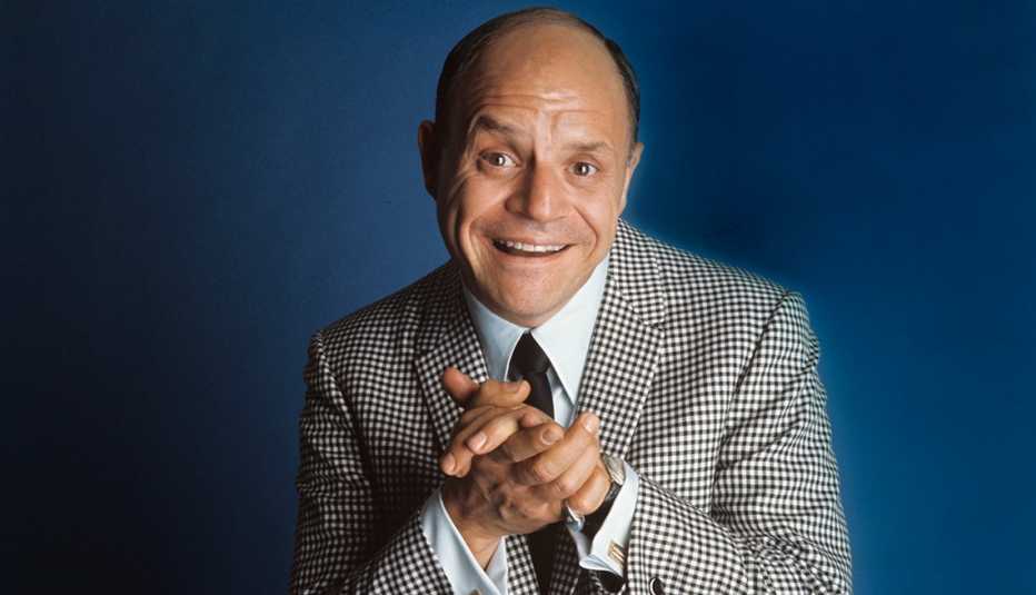 comedian don rickles smiling and clasping his hands together on a blue field