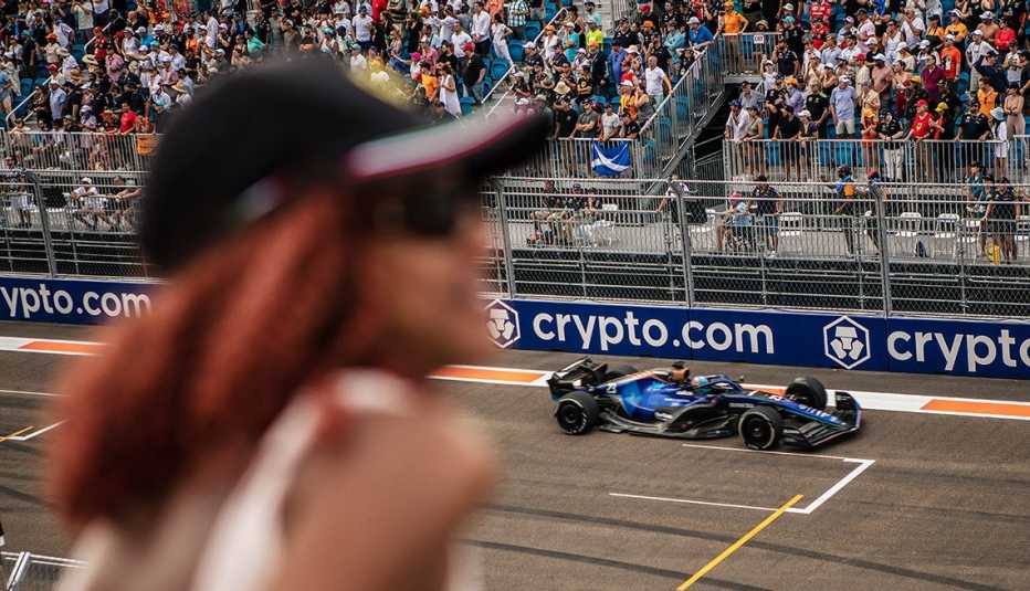 a blue formula one car is in focus with a woman in the foreground on a track in miami