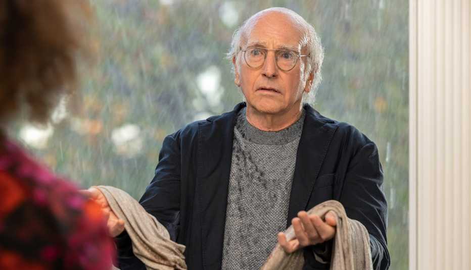 Larry David standing in a doorway with rain pouring behind him in "Curb Your Enthusiasm."