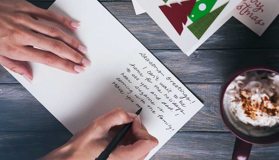 a woman writes a holiday card on a table with other cards