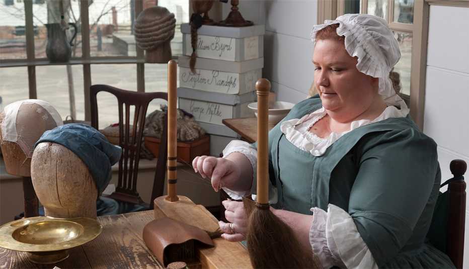 a colonial williamsburg worker in period specific dress makes a wig