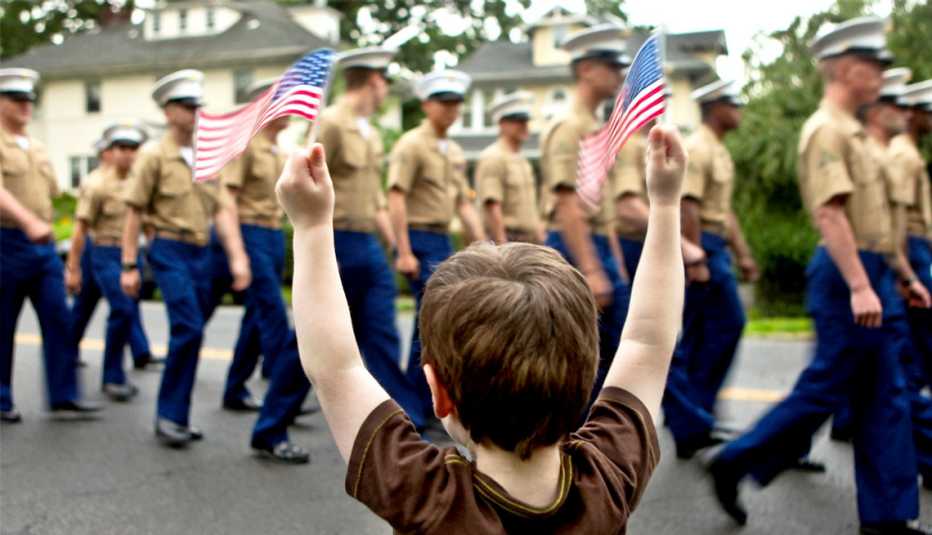 a young boy holds up miniature american flags at a military parade