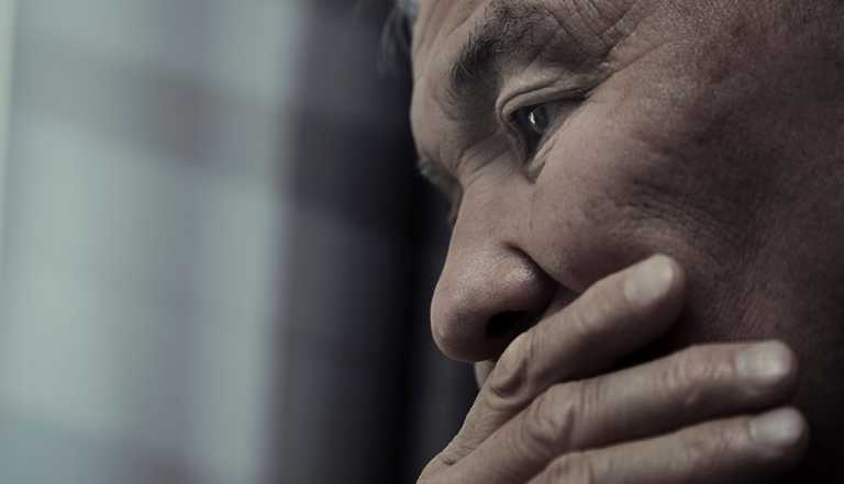 extreme close up of a depressed man holding his face in his hand on a gray background to reflect the rising rate of suicide in older adults namely men