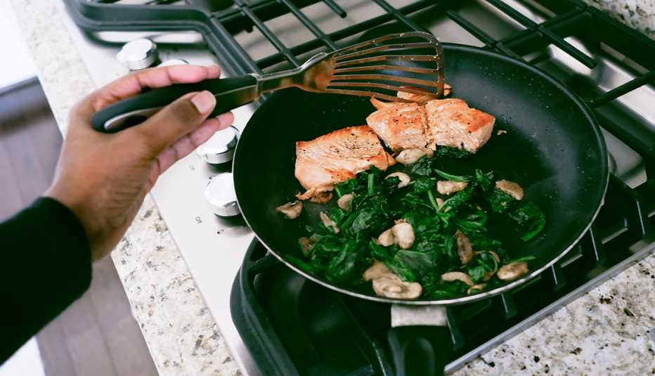 woman cooking salmon with spinach and mushrooms in a pan on stove