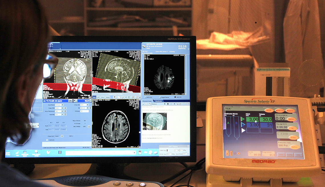 a technician looks at a monitor screen of brain scans and an m r i instrument panel