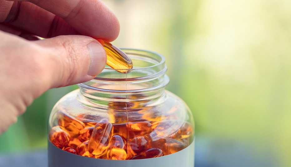 A person taking a fish oil capsule from a pill bottle