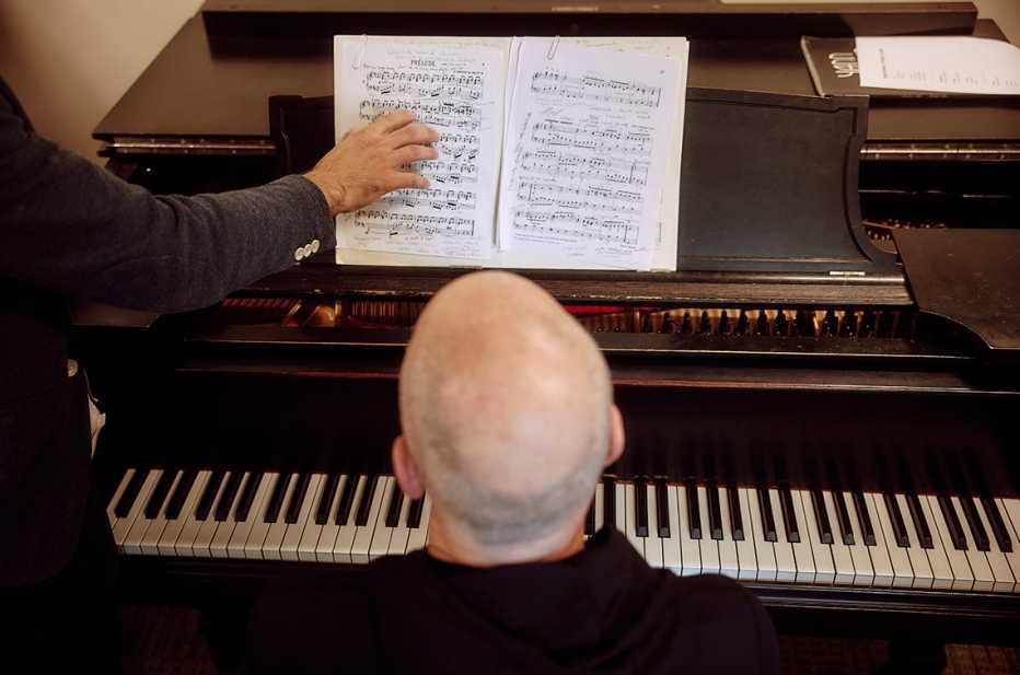 overhead shot of the top of jeffrey galvins head while he is sitting at the piano and his teachers hand is pointing out a section showing on the music stand above the keyboard