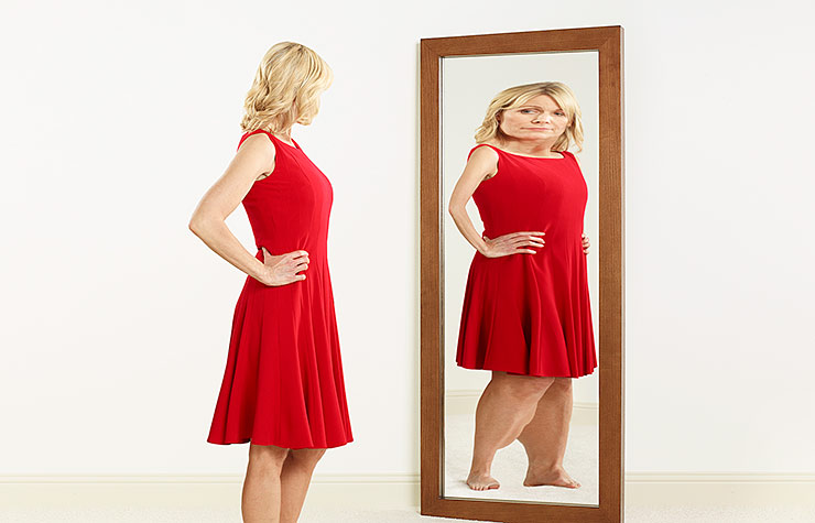 A woman with an eating disorder looks at her warped reflection in a mirror.