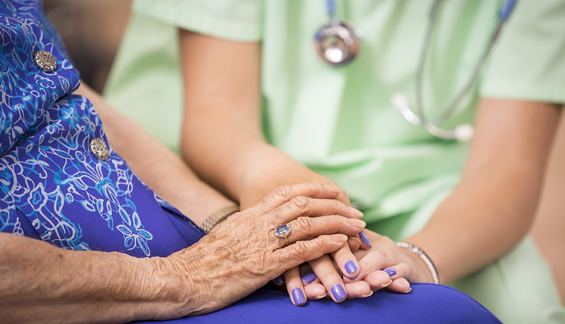 Close-up of older female patient in nursing home holding hands with her nurse.