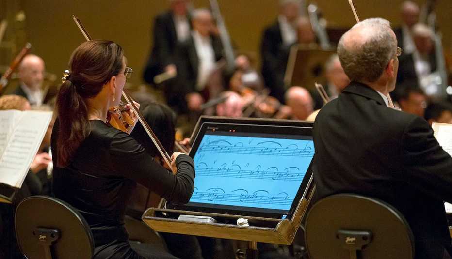 Alison Dalton playing violin with the Chicago Symphony Orchestra 125th Year.Chicago Symphony Orchestra. In front of her is a computerized monitor with enlarged sheet music. 