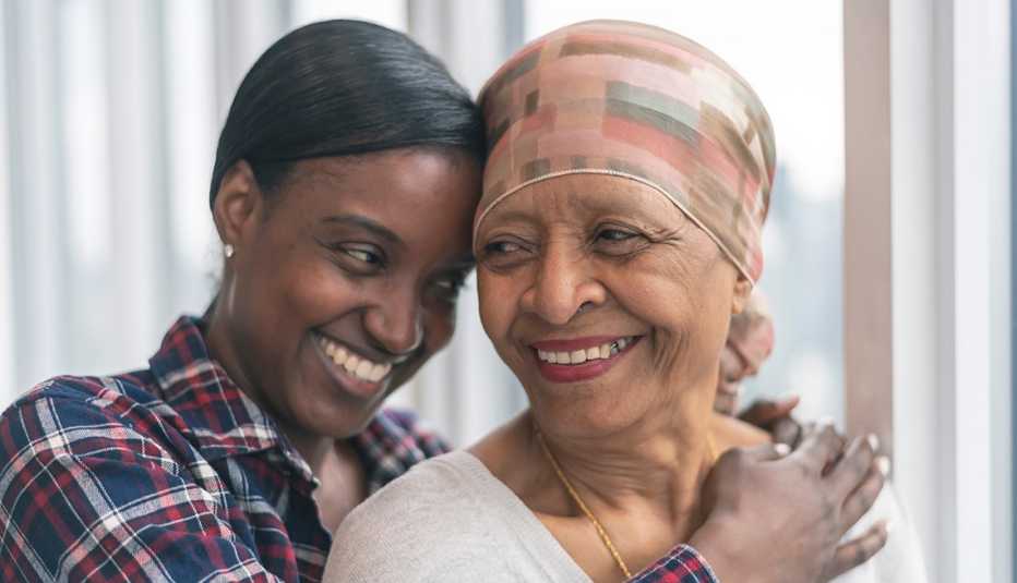 A woman with cancer is wearing a scarf on her head as her adult daughter is giving her a hug. Both women are smiling with gratitude and hope for recovery.
