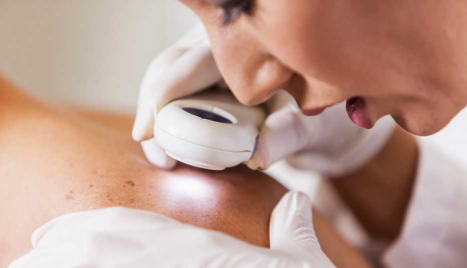 Female dermatologist examining patient's skin with dermascope for signs of skin cancer.