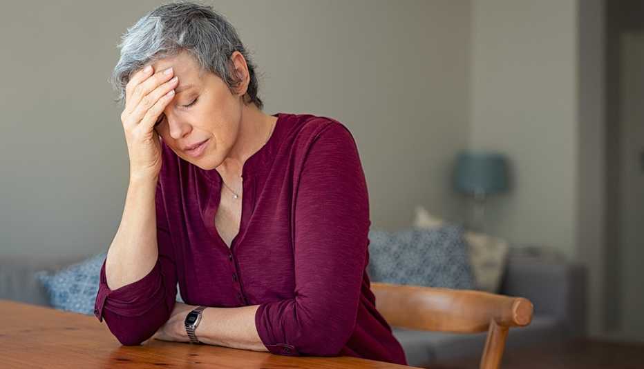 Senior woman suffering from headache and depressed while sitting at table in a living room. 